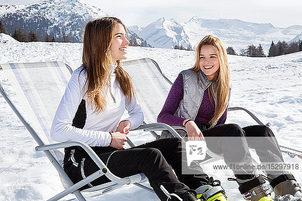Zwei jugendliche Skifahrerinnen sitzen in Liegestühlen in schneebedeckter Landschaft  Tirol  Steiermark  Österreich