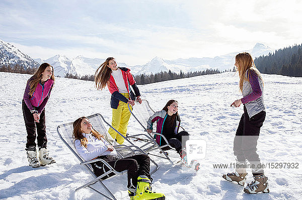 Fünf jugendliche Skifahrerinnen im Stehen und in Liegestühlen in verschneiter Landschaft  Tirol  Steiermark  Österreich