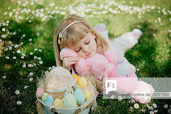 Süßes Mädchen im Gras liegend mit Spielzeugkaninchen und Ostereierkorb