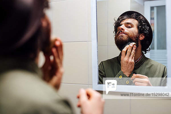 Bärtiger junger Mann beim Bartstreichen im Badezimmer