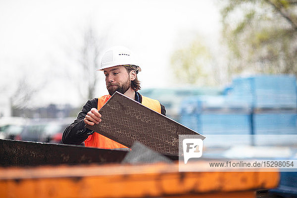 Mittelgroßer erwachsener männlicher Bauarbeiter  der Abfall in den Abfallcontainer wirft