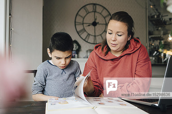 Mutter liest zu Hause Geschichte aus Bilderbuch für autistischen Sohn