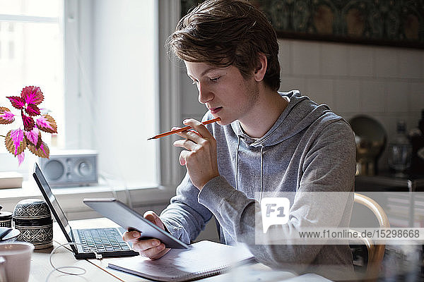 Serious teenage boy using digital tablet while doing homework on table