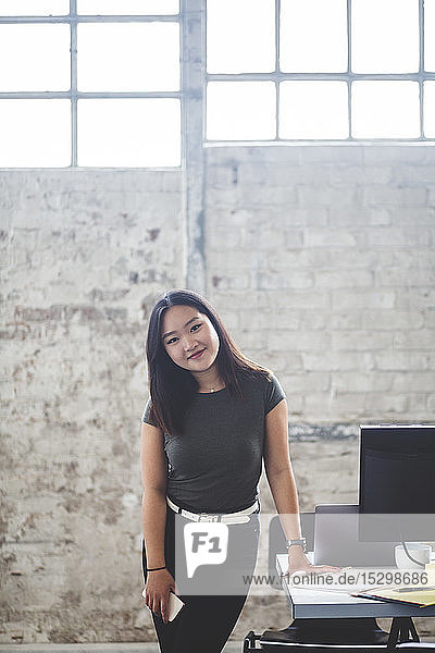 Porträt einer selbstbewussten Computerprogrammiererin  die im Kreativbüro neben dem Schreibtisch steht
