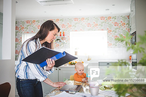 Multi-Tasking-Telearbeit der Mutter  während die Tochter am Esstisch in der Küche sitzt