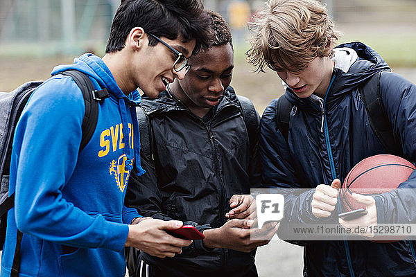 Freunde unterhalten sich beim Blick auf das Smartphone auf dem Spielfeld
