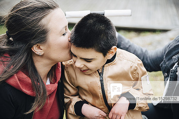 Mutter küsst behinderten Sohn  der auf einem Rollstuhl im Hof sitzt