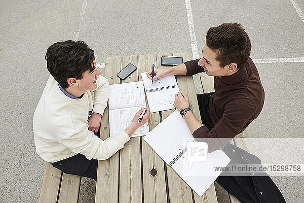 High angle view of teenage boys smiling while studying at table in schoolyard