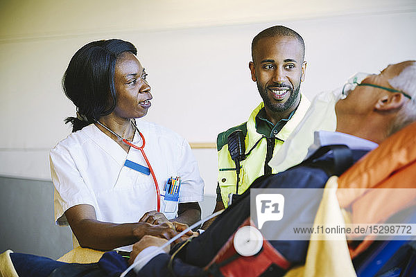 Arzt im Gespräch mit Sanitäter während Behandlung eines reifen Geschäftsmannes auf Krankenhausbahre