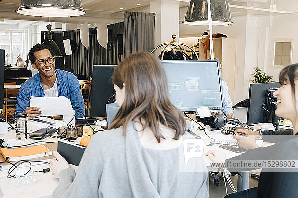 Fröhliche männliche und weibliche IT-Fachleute unterhalten sich am Schreibtisch im Kreativbüro