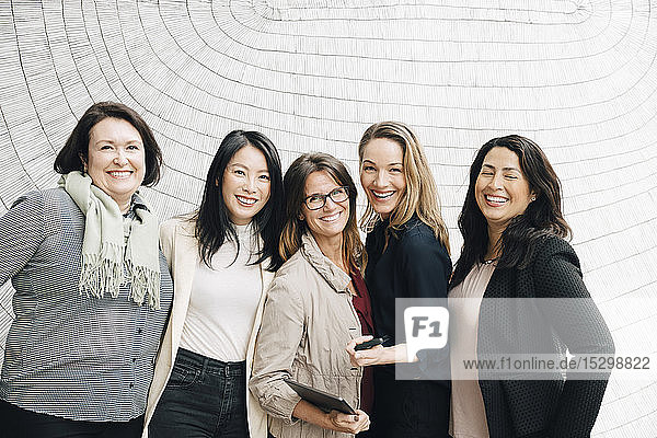 Portrait of smiling multi-ethnic businesswomen standing against wall at workplace