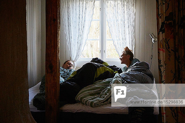 Männliche und weibliche Freunde unterhalten sich  während sie sich zu Hause im Bett am Fenster entspannen