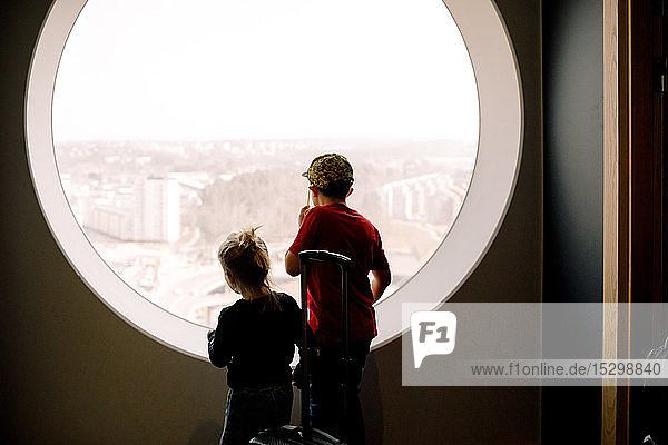 Geschwister schauen durch das Fenster  während sie im Hotelzimmer stehen