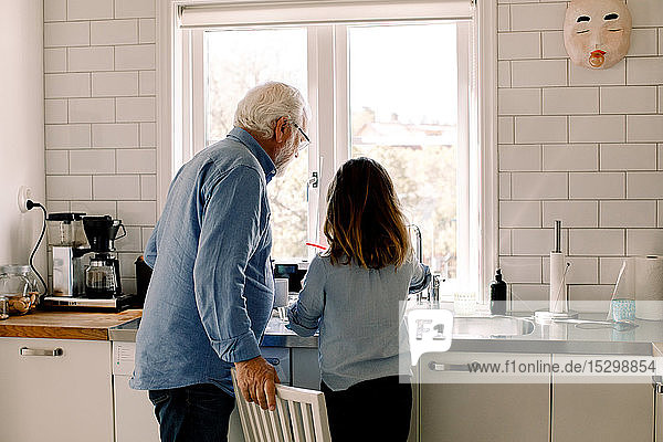 Grandfather and granddaughter standing at counter in kitchen