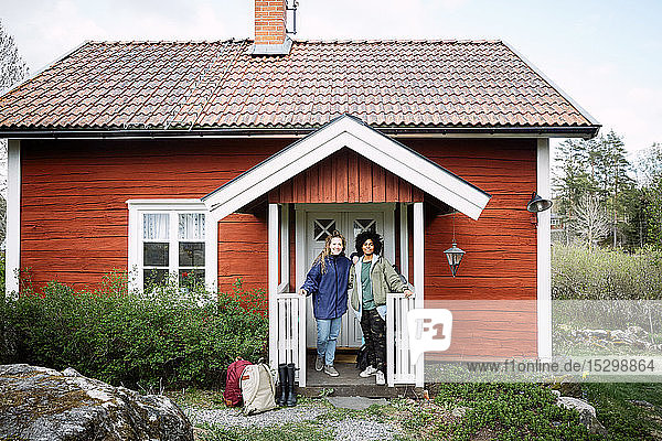 Porträt von lächelnden Freundinnen mit Rucksäcken  die am Wochenende vor der Hütte stehen