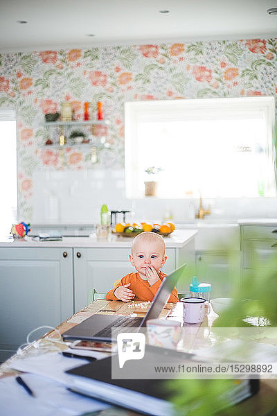Kleines Mädchen schaut weg  während es am Esstisch in der Küche im Heimbüro sitzt