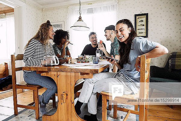 Porträt einer lächelnden jungen Frau  die ein Smartphone benutzt  während sie mit Freunden zu Hause sitzt