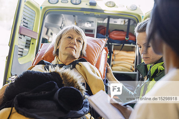 Reife Patientin auf Krankenhausbahre schaut Arzt gegen Krankenwagen an
