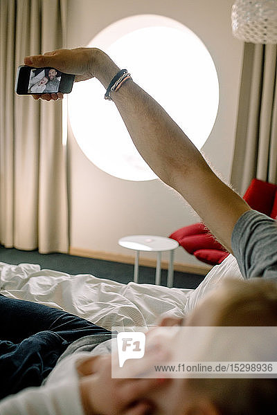 Father taking selfie with daughter on bed in hotel