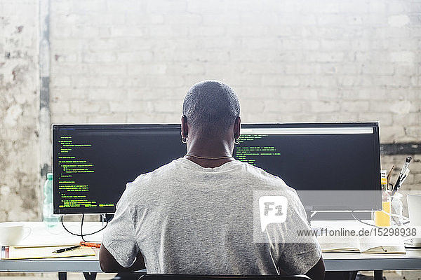 Rückansicht eines männlichen IT-Experten bei der Arbeit am Computer während der Codierung am kreativen Arbeitsplatz