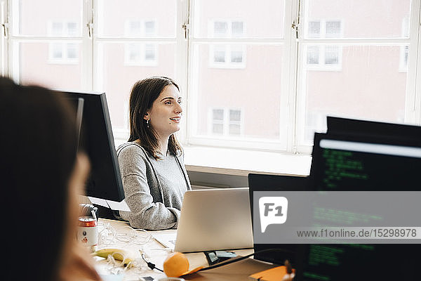 Smiling female computer programmer looking away while sitting at desk in office
