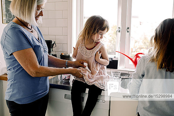 Grandmother cleaning granddaughter's dress by girl working at counter in kitchen