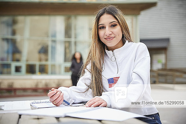 Porträt eines selbstbewussten Teenagers  der am Tisch auf dem Schulhof sitzt
