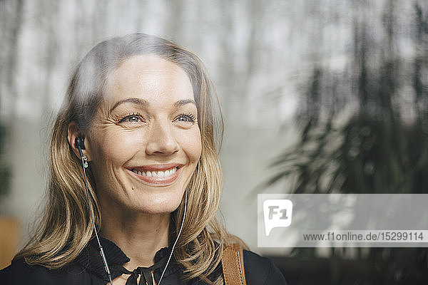 Lächelnde blonde Geschäftsfrau  die über Kopfhörer Musik hört  während sie im Büro wegschaut