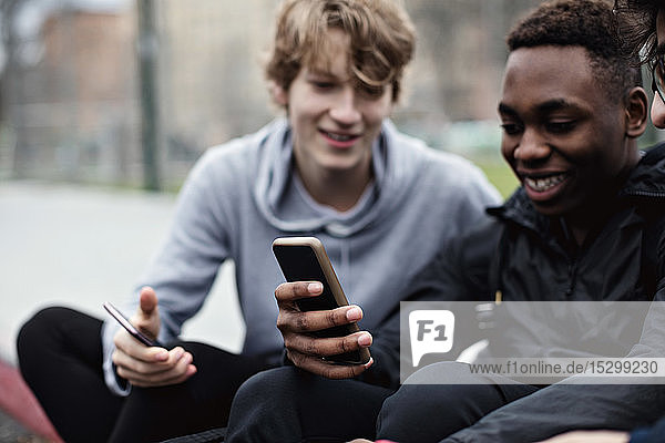Phone addictive happy friends sitting on sidewalk in city
