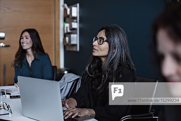 Geschäftsfrau schaut weg  während sie den Laptop am Schreibtisch im Büro benutzt