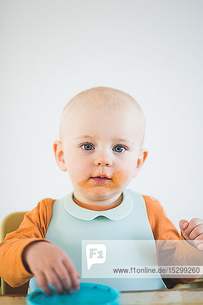 Portrait of baby girl with bib and messy mouth sitting at home