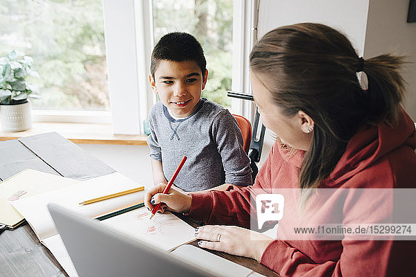 Mother teaching drawing to autistic son while sitting at home