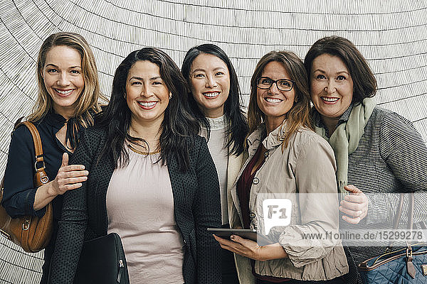 Porträt von lächelnden multiethnischen Geschäftsfrauen  die am Arbeitsplatz an der Wand stehen
