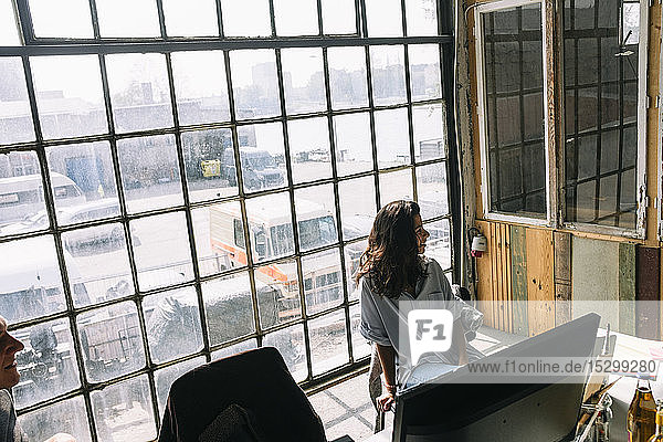 Junge Geschäftsfrau sitzt auf Stuhl gegen Fenster im Sitzungssaal am kreativen Arbeitsplatz