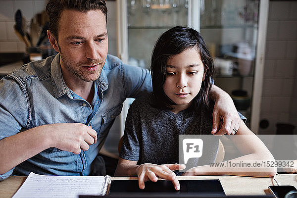 Son using laptop by father while doing homework at home