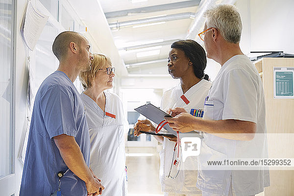 Männliche und weibliche Ärzte diskutieren über ein digitales Tablett  während sie im Krankenhaus auf dem Flur stehen