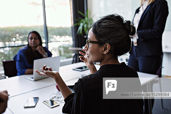 Businesswoman gesturing while discussing with colleagues during meeting at conference table in board room
