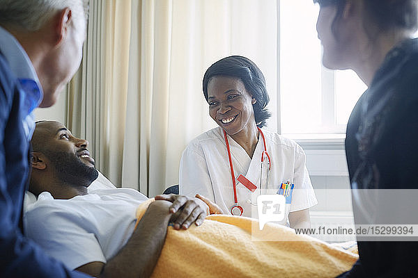 Lächelnde Ärztin im Gespräch mit Patient und Familie auf der Krankenhausstation