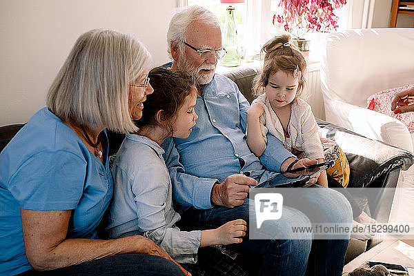 Großeltern und Enkelkinder benutzen digitales Tablet  während sie zu Hause im Wohnzimmer sitzen