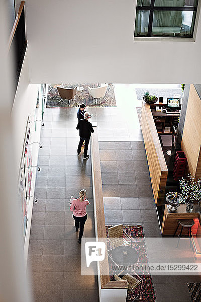 High angle view of businesswoman walking towards colleagues standing in corridor at office