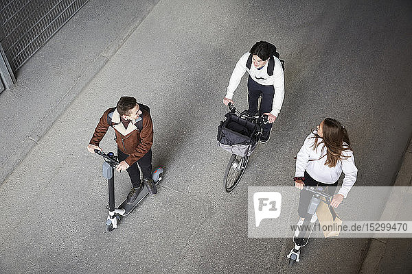 High angle view of male and female friends riding electric push scooters and bicycle on road in city