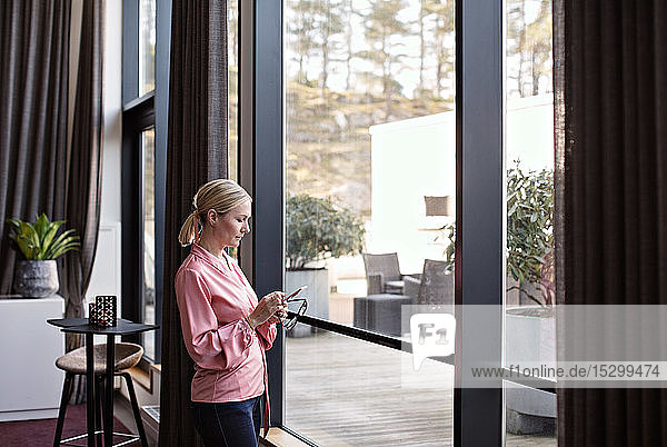 Businesswoman using phone while standing by window in office