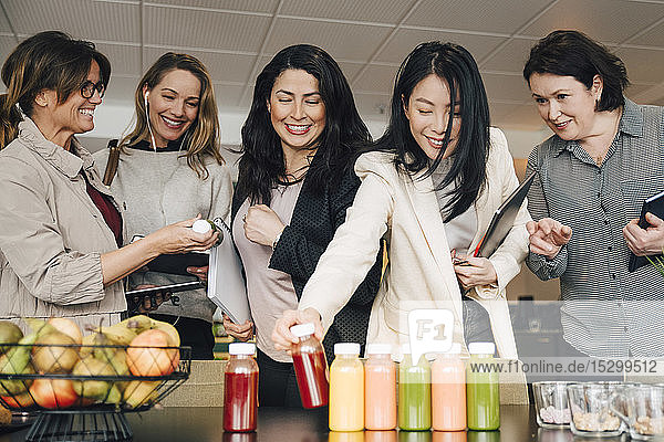 Lächelnde multiethnische Geschäftsfrauen schauen bei Veranstaltungen auf Saftflaschen auf dem Tisch