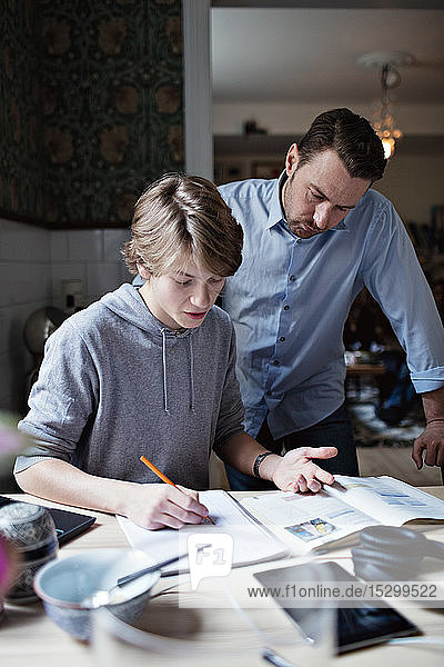 Father looking at son doing homework on table
