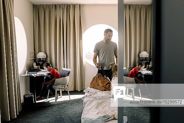Mann hält Tasche ans Bett  während Junge im Hotel am Tisch sitzt