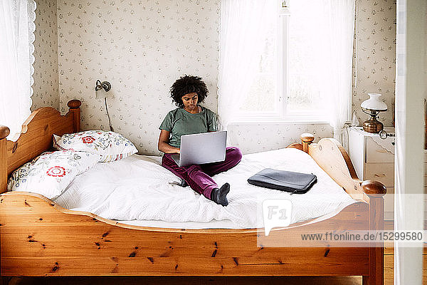 Hochwinkelansicht einer jungen Frau  die einen Laptop benutzt  während sie sich zu Hause auf dem Bett entspannt  durch die Tür gesehen