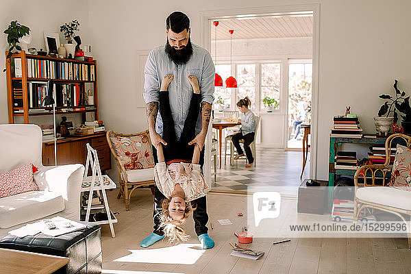 Playful father swinging girl while standing in living room at home