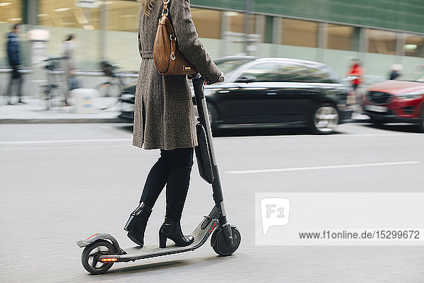 Low section of businesswoman riding electric push scooter on street in city