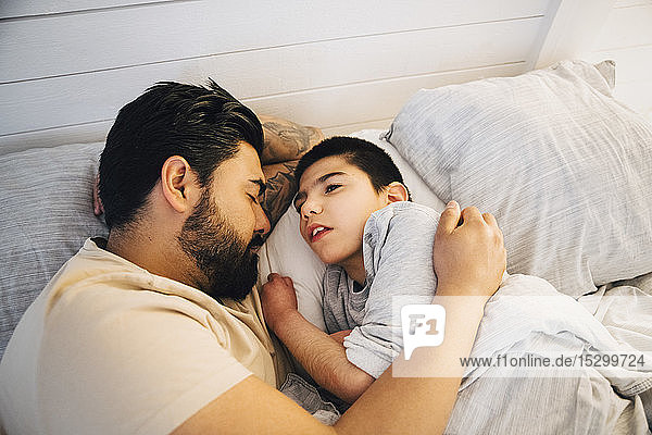 High angle view of father with disable son lying on bed at home