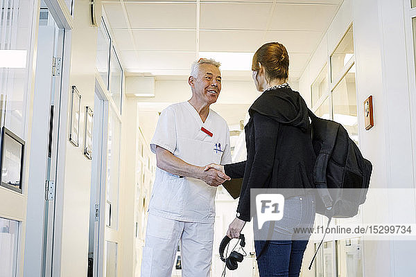 Männlicher Arzt schüttelt Patientin bei Routineuntersuchung in medizinischer Klinik die Hand